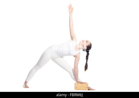 Sportlich schöne junge Anfang Yoga Studentin stehen in Utthita Trikonasana, erweitert Dreieck darstellen mit Holzblock Stockfoto