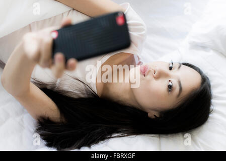 Frau im Bett liegend, mit Smartphone, ein Selbstporträt zu nehmen Stockfoto