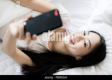 Frau im Bett liegend, mit Smartphone, ein Selbstporträt zu nehmen Stockfoto