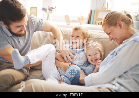 Glückliche junge Eltern spielen mit niedlichen Kinder auf sofa Stockfoto