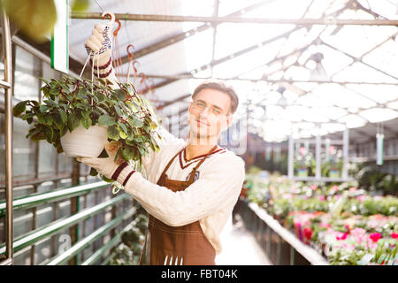 Lächelnder Mann Gärtner arbeiten und hängenden Blumen in Töpfen im Garten-center Stockfoto