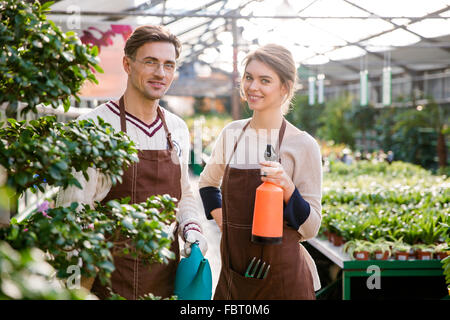Glücklich Mann und Frau Gärtner halten Gießkanne und Pulverisierer für das Sprühen von Blumen und Pflanzen im Gewächshaus Stockfoto