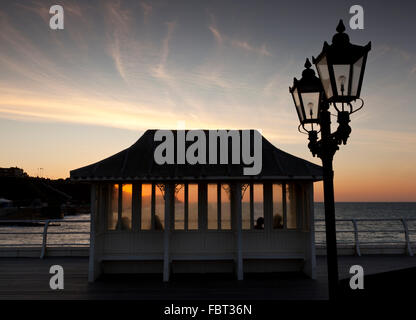 Vier Personen in einem der viktorianischen Zierpflanzen Unterstände auf Cromer Pier, Norfolk, England, UK sitzen, den Sonnenuntergang zu beobachten. Stockfoto