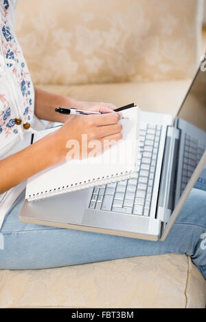 Nahaufnahme von Frau schreiben auf Notizblock mit Laptop auf den Beinen Stockfoto