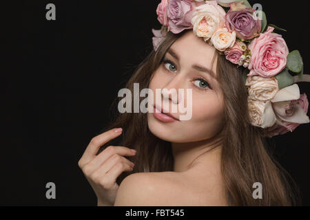 Porträt einer schönen Frau mit Kranz aus Blumen auf Kopf posieren auf schwarzem Hintergrund Stockfoto