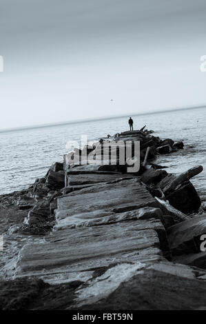 Einsame Gestalt des Menschen auf der Mole mit Blick auf See.  Cooles getönten Bild in schwarz und weiß. Stockfoto