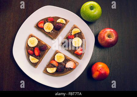 Pfannkuchen in vier Teile geschnitten dekoriert mit Früchten, flankiert von zwei Äpfel und Pfirsich Stockfoto