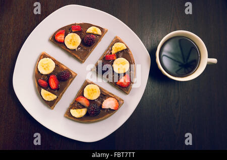 Pfannkuchen in vier Teile geschnitten dekoriert mit Früchten, flankiert Tasse Kaffee Stockfoto