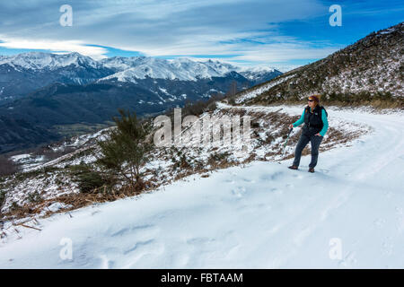Frau in schwarz auf Schnee und Eis bedeckten Straße mit weit entfernten schneebedeckten Pyrenäen Stockfoto