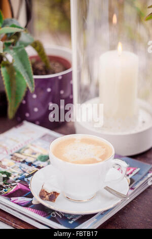 Tisch mit Kaffee, süß, Zeitschriften, Laterne mit brennender Kerze und Haus Pflanze Stockfoto