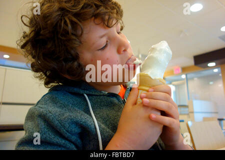 ein 8 Jahre alter Junge lecken und Essen ein Eis Stockfoto