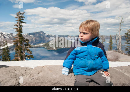 Kleiner Junge sitzt im Crater Lake Nationalpark in Oregon, USA Stockfoto