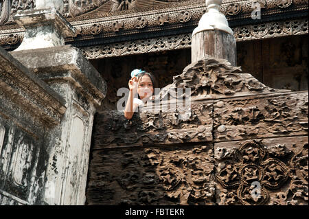 Burmesische Mädchen Kollegen über die Holzwände vor der aus Teakholz geschnitzte Wand der Shwenandaw Kyaung Pagode in Mandalay Myanmar Stockfoto