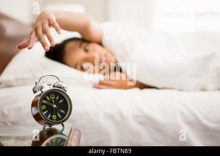 Wecker gegen Brünette auf Bett Stockfoto