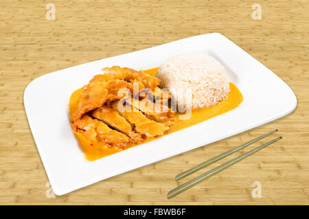 Chinesisches Essen auf eine weiße Platte stehend in einer Tabelle. Gebratene Ente mit Reis und Kokosnuss-Sauce. Hintergrund Holz mit Stäbchen. Stockfoto