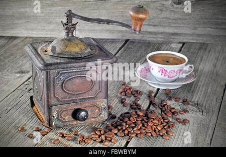 Alte Kaffeemühle, Kaffeebohnen und Tasse Kaffee auf einem Holztisch Stockfoto