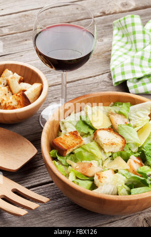 Frische gesunde Caesar Salat und Rotweinglas auf Holztisch Stockfoto