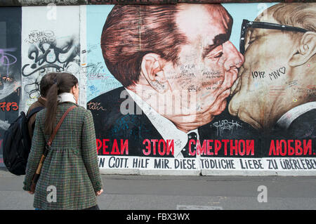 Touristen, die Anzeigen von Bildmaterial auf der Berliner Mauer an der East Side Gallery zeigt einen Kuss zwischen Leonid Brezhnev und Erich Honecker Stockfoto
