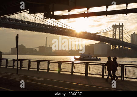 Zwei Frauen gehen nördlich an der East River Esplanade beim Sonnenaufgang über Manhattan Bridge New York City Stockfoto