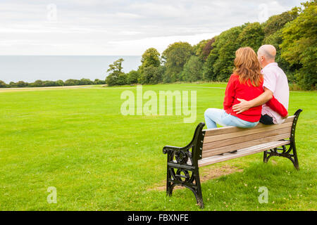 Rückansicht des mittleren Alters paar sitzt auf einer Bank mit Blick auf das Meer Stockfoto