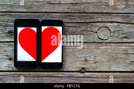 Zwei Handys mit halben Herzsymbol auf hölzernen Hintergrund Stockfoto