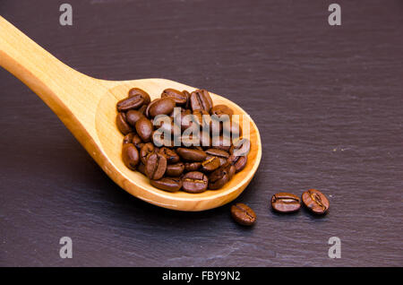 Kaffeebohnen in Holzlöffel auf Schiefer Stockfoto
