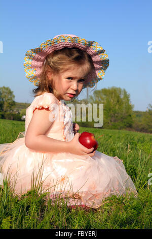 kleine Mädchen essen Apfel auf Wiese Stockfoto