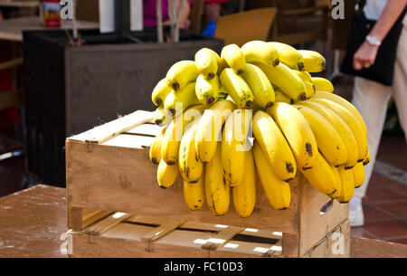 Cluster für gelbe Bananen auf Holzkiste mit Menschen zu Fuß durch an sonnigen Tag auf der Straße Stockfoto