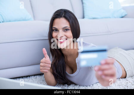 Lächelnde schöne Brünette auf dem Boden liegend und Online-Einkäufen Stockfoto