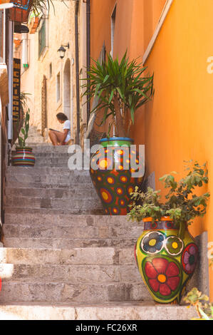 Mann, der allein liest, Blick auf einen Mann, der in einer engen Straße in der Altstadt von Taormina, Sizilien, Italien, ein Buch liest. Stockfoto