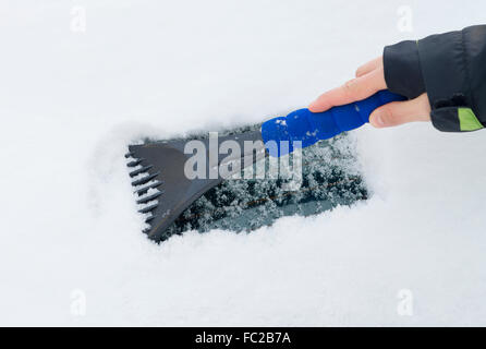 Hand von einer Frau kratzen Schnee und Eis von der Auto-Windschutzscheibe Stockfoto