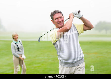 Glücklich Golfer mit Partner hinter ihm Abschlag Stockfoto