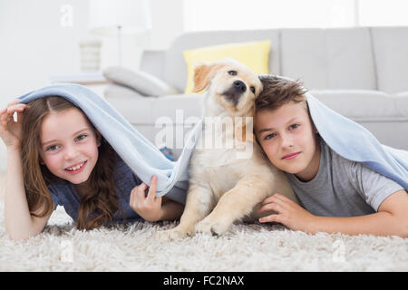 Niedlichen Geschwister mit Hund unter der Decke im Wohnzimmer Stockfoto