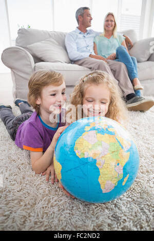 Kinder erkunden Globus während die Eltern auf sofa Stockfoto