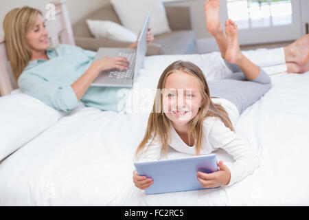 Mutter mit Laptop während Tochter mit TabletPC auf dem Bett Stockfoto