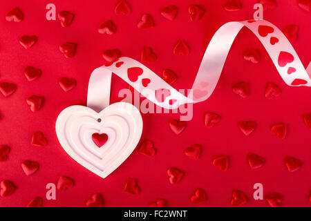 weiße Form Herz mit Band und roten Herzen auf rotem Grund. Valentinstag-Konzept. Stockfoto