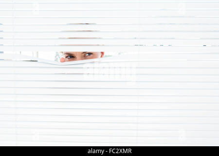 Neugierig blonde Frau auf der Suche durch Jalousie Stockfoto