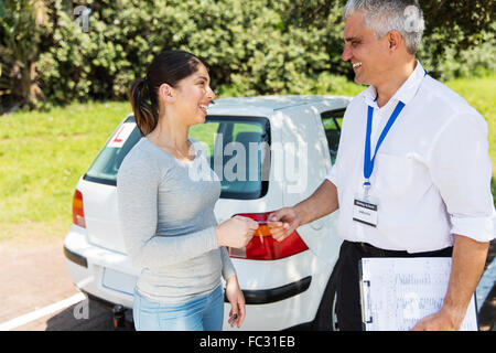 fröhliche junge Frau, die den Führerschein durch senior Fahrlehrer übergeben wird Stockfoto