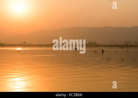 Goldener Sonnenuntergang am Ana Sagar See in Ajmer, Indien mit Silhouetten der Bäume und Fischer. Stockfoto
