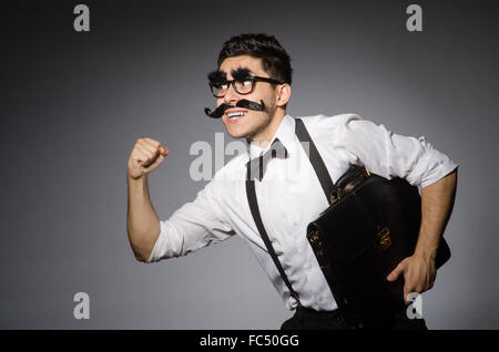 Junger Mann mit falschen Schnurrbart hält Fall isoliert auf grau Stockfoto