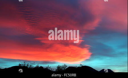 Dramatische Wolken bei Sonnenuntergang mit Hügeln und Bäumen in der Silhouette. Stockfoto