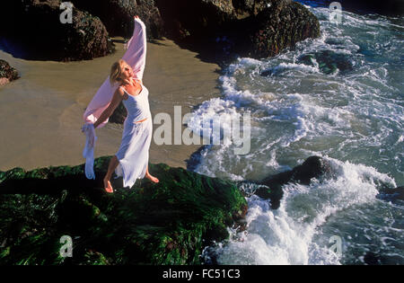 Frau im weißen Kleid Lebensfreude auf Welle fegte Felsenufer in Kalifornien Stockfoto