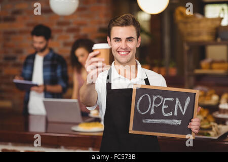 Lächelnd Barista mit Take-away-Becher und Schild "geöffnet" Stockfoto
