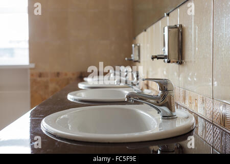 Das Wasser fließt aus dem Hahn in einer öffentlichen Toilette. Niemand hier. Abfall und unangemessene Nutzung. Stockfoto