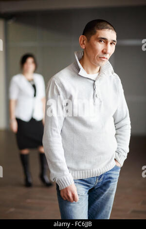 Applying Mann in Freizeitkleidung mit kurzen Haaren nachdenklich schauen direkt in die Kamera, der Mitarbeiter bekommt Job. Im Hintergrund Personalleiter Frau tragen weißen Anzug und strenge Schwarz Kleid wartet. Stockfoto