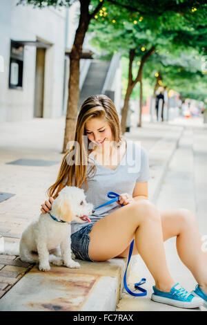 Kaukasische Frau Petting Hund auf Bürgersteig Stockfoto