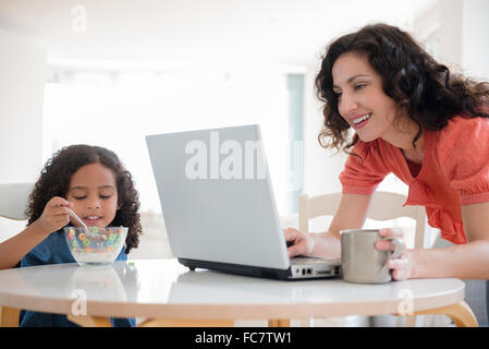 Mutter mit Laptop beim Frühstück mit Tochter Stockfoto