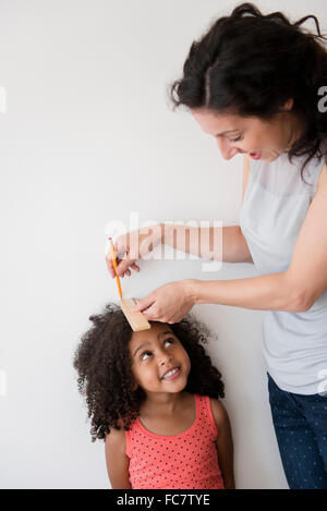 Mutter, die Messung der Höhe der Tochter gegen Wand Stockfoto