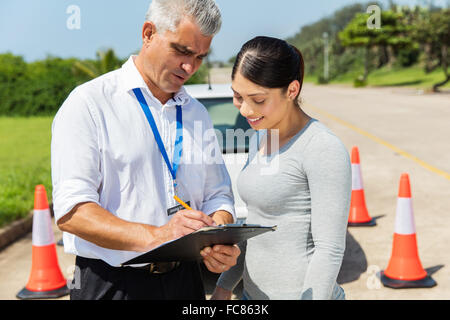 glückliche Schüler Fahrer mit senior Instruktor, Ausfüllen von Formularen vor der Fahrprüfung Stockfoto