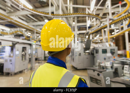 Arbeiter in Akkubohrschrauber beobachten Druckmaschine Förderbänder und Maschinen in Druckerei Stockfoto